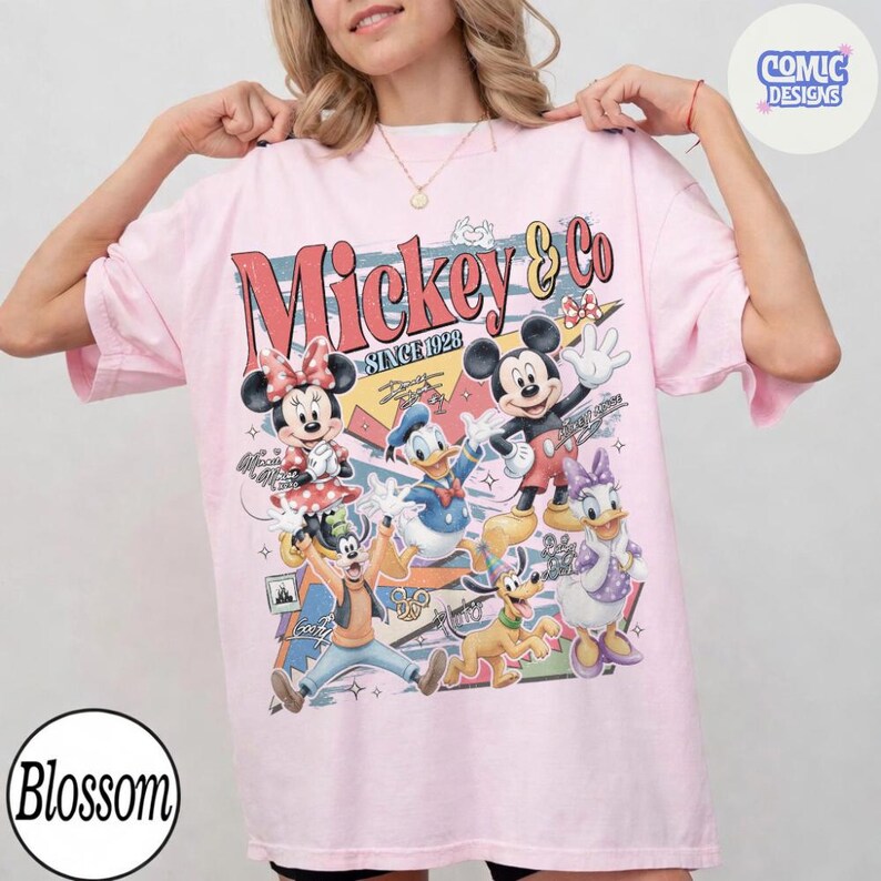 May include: Pink t-shirt featuring a colorful graphic of Mickey Mouse and friends. The design includes Mickey, Minnie, Donald Duck, Daisy Duck, Goofy, and Pluto, with the text "Mickey & Co SINCE 1928".