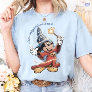May include: Pale blue t-shirt with a cartoon Mickey Mouse as a wizard, holding a wand with a sparkling effect. Mickey is in a blue wizard hat with stars and a red robe. The text "Some imagination huh?" is arched above the character.