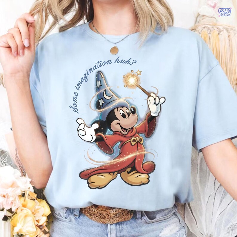 May include: Pale blue t-shirt with a cartoon Mickey Mouse as a wizard, holding a wand with a sparkling effect. Mickey is in a blue wizard hat with stars and a red robe. The text "Some imagination huh?" is arched above the character.