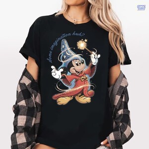 May include: Black t-shirt with a cartoon Mickey Mouse wizard design, holding a wand with a sparkling effect. The text "Some imagination huh?" is arched above the character. The design is in vibrant colours.