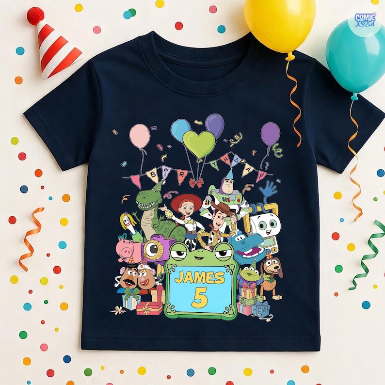 May include: A navy blue short-sleeve t-shirt featuring a colorful graphic of various animated toy characters, balloons, and a banner that reads BIRTHDAY. A central green frog-shaped frame contains the text JAMES and the number 5.