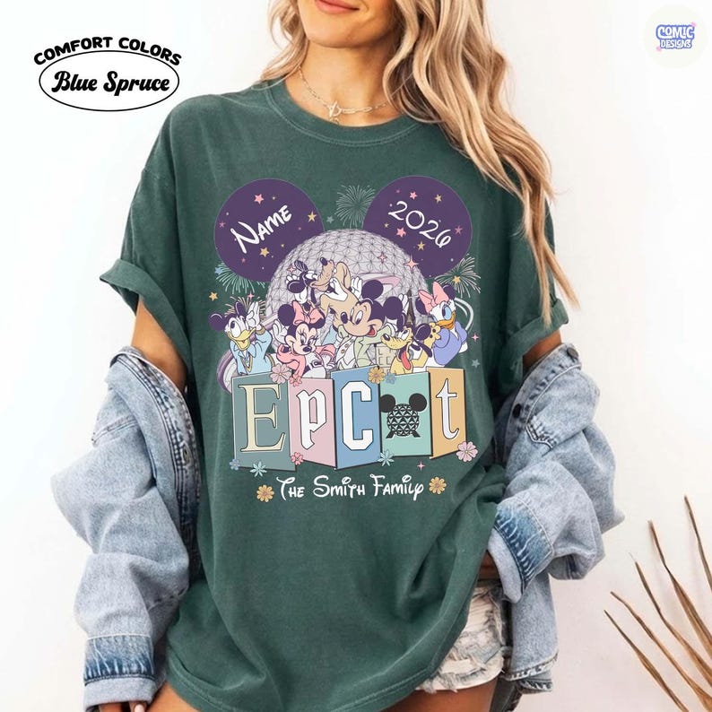 May include: Dark green t-shirt with a graphic featuring Disney characters, the word "EPCOT" in colorful blocks, and the text "The Smith Family". The design includes the text "Name" and "2026" in purple Mickey Mouse ears. The shirt has the "Comfort Colors" and "Blue Spruce" logo.