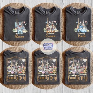May include: Six charcoal gray t-shirts featuring Disney character graphics. The top row shows Sulley, Chip and Dale, and Lightning McQueen with names Bruno, Clover, and Kallie. The bottom row displays a group of characters with the text Family Trip Paris.