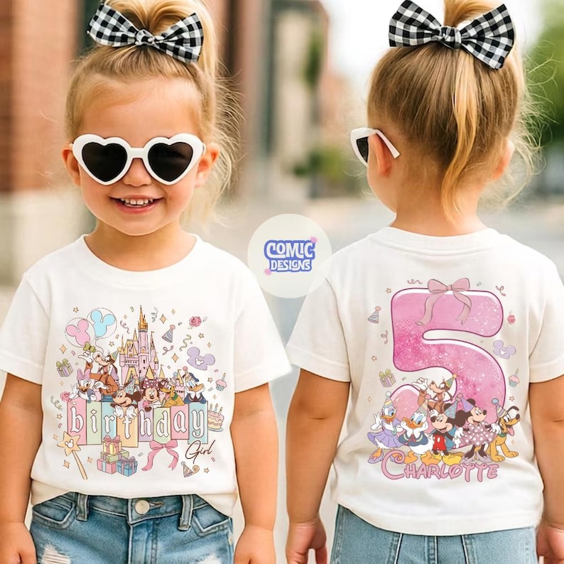 May include: A white t-shirt featuring a colorful graphic of a castle, balloons, and cartoon characters. The text "Birthday Girl" is displayed. The back of the shirt shows a pink number 5 with cartoon characters and the name "Charlotte".