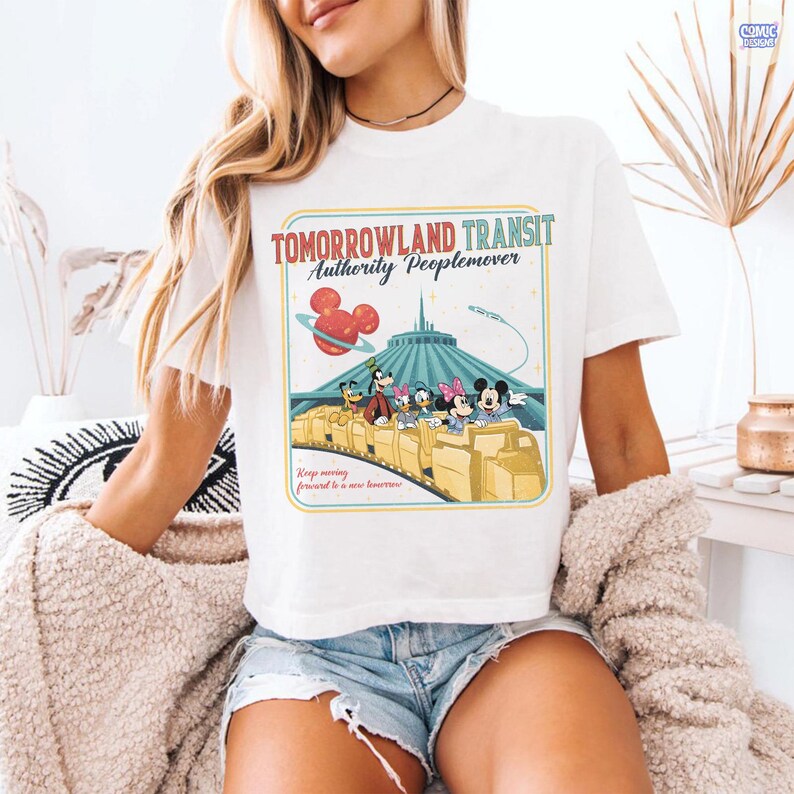 Puede incluir: Camiseta blanca con un gr&aacute;fico retro de la atracci&oacute;n Tomorrowland Transit Authority Peoplemover. El dise&ntilde;o incluye a Mickey Mouse, Minnie Mouse, Donald Duck, Daisy Duck y Goofy en el Peoplemover. La camiseta tiene el texto "Tomorrowland Transit Authority Peoplemover".