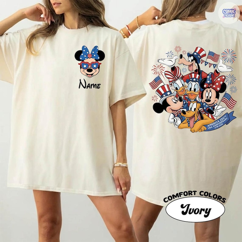 May include: Ivory-colored t-shirt featuring a Minnie Mouse graphic with a patriotic bow and sunglasses. The back of the shirt displays a group of Disney characters with American flags and fireworks. The text "Name" is printed on the front.