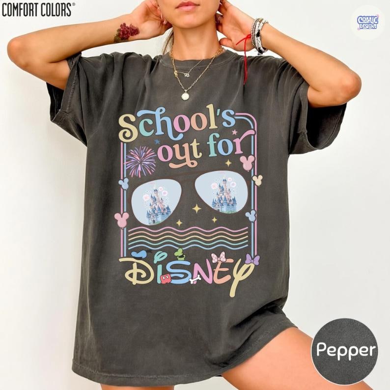 Może przedstawiać: Koszulka w kolorze pieprzu z napisem "School's Out for Disney" w kolorowych literach. Projekt zawiera okulary przeciwsłoneczne z obrazem zamku, fajerwerki i ikony Myszki Miki. Koszulka marki Comfort Colors.