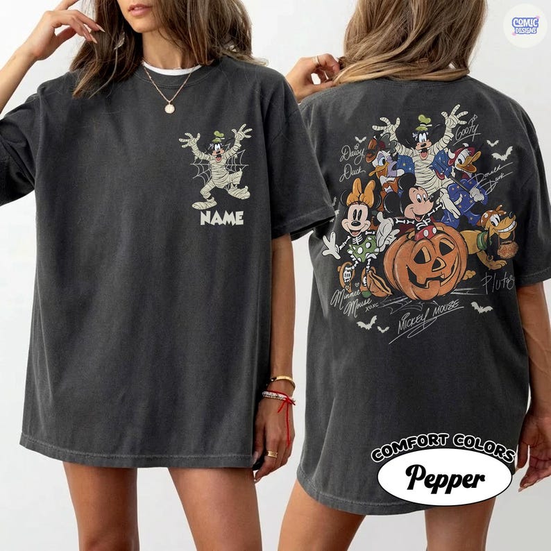 May include: A charcoal gray short-sleeve t-shirt featuring a front graphic of Goofy as a mummy with a spiderweb and the word NAME. The back displays a large Halloween-themed illustration of Disney characters including Mickey, Minnie, and Pluto.