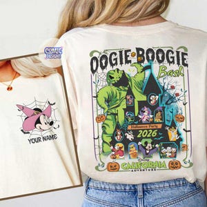 May include: Cream-colored t-shirt featuring a colorful graphic for the "Oogie Boogie Bash" Halloween party at Disney California Adventure in 2026. The design includes the Oogie Boogie character, a haunted house, and various Disney characters.