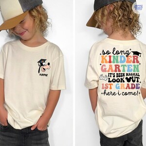 May include: Cream-colored t-shirt with a cartoon image of a dog wearing a graduation cap and the name "NAME" below it. The back of the shirt has the text "so long KINDERGARTEN, IT'S BEEN MAGICAL, LOOK OUT 1ST GRADE +here i come!+"