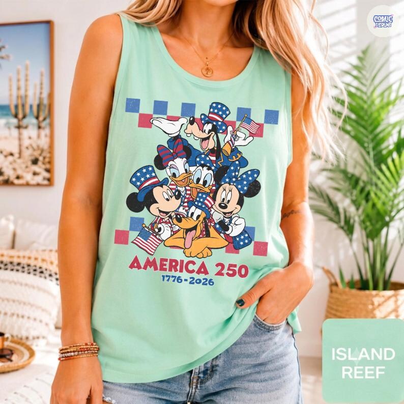 May include: A light green sleeveless tank top featuring a graphic of cartoon characters wearing patriotic hats and holding American flags. The text reads AMERICA 250 and 1776-2026, set against a red and blue checkered background pattern.