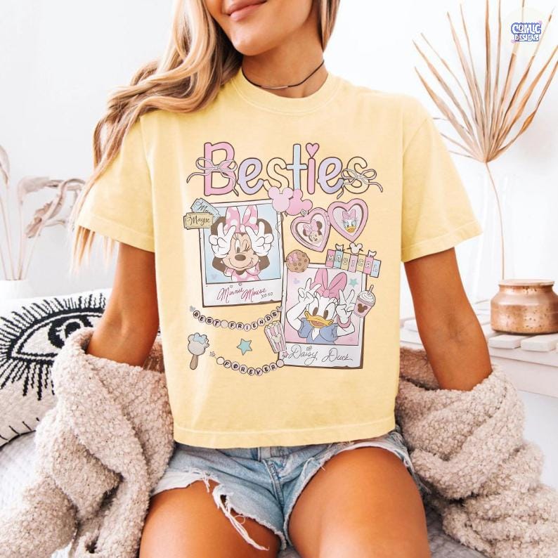 Puede incluir: Camiseta amarilla clara con la palabra "Besties" en escritura rosa y morada. La camiseta presenta im&aacute;genes de Minnie Mouse y Daisy Duck en marcos estilo polaroid, con elementos decorativos.