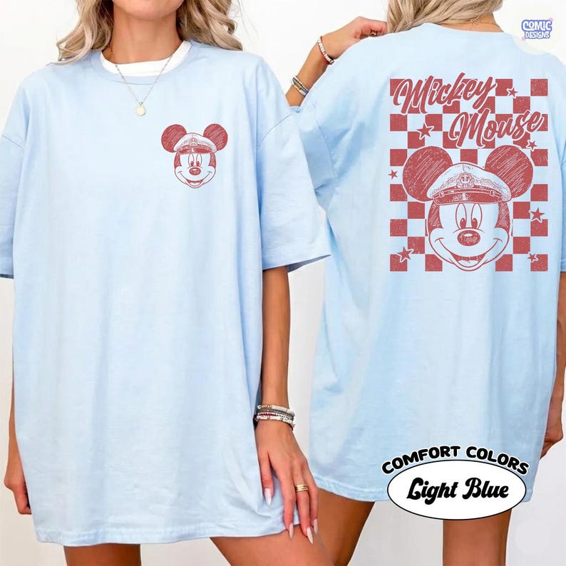 May include: Pale blue t-shirt with a red Mickey Mouse design on the front and back. The back of the shirt displays "Mickey Mouse" over a red and white chequered pattern. The shirt is labelled "Comfort Colors" and "Light Blue".