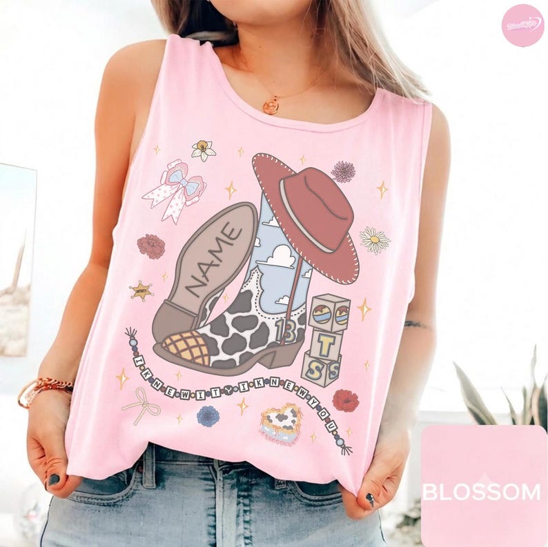 Puede incluir: Una camiseta sin mangas de color rosa claro con un estampado gr&aacute;fico de una bota vaquera con estampado de vaca, un sombrero marr&oacute;n, un lazo, flores y bloques apilados con las letras T, S y la palabra NAME. Un collar de cuentas dice I KNEW IT Y I KNEW IT Y.