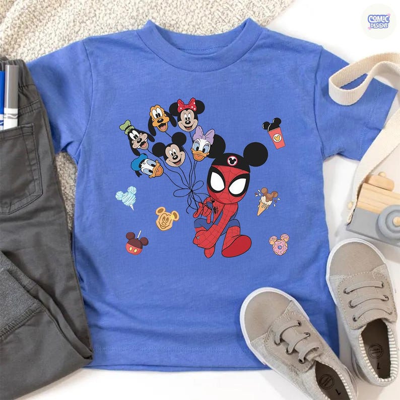Peut inclure: Un t-shirt bleu clair avec un personnage de dessin anim&eacute; Spider-Man avec des oreilles de Mickey Mouse tenant des ballons avec des visages de personnages Disney. Le t-shirt est pr&eacute;sent&eacute; avec un pantalon gris et des baskets en toile.