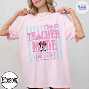 May include: A light pink t-shirt with the words "TEACHER MODE" in pink, and a Minnie Mouse graphic. The design includes blue vertical stripes and a bow. The word "OFF" is below the Minnie Mouse graphic.