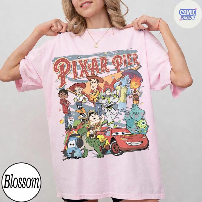 Pu&ograve; includere: Una maglietta rosa chiaro con una grafica colorata di vari personaggi Pixar, tra cui Woody, Buzz Lightyear e Saetta McQueen. Le parole "Pixar Pier" sono stampate sopra i personaggi in un font retr&ograve;. La maglietta ha maniche corte e una vestibilit&agrave; ampia.