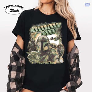 May include: Black t-shirt featuring a graphic from "The Mandalorian" with the text "The Mandalorian and Grogu" and "This is the Way." The design includes images of the Mandalorian, Grogu, and spacecraft. The shirt is labeled "Comfort Colors."