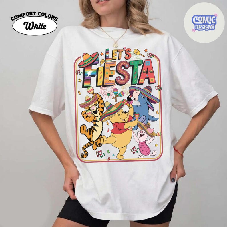 May include: White t-shirt with a colorful "Let's Fiesta" graphic featuring cartoon characters wearing sombreros and playing maracas. The shirt has the "Comfort Colors" and "Comic Designs" logos.