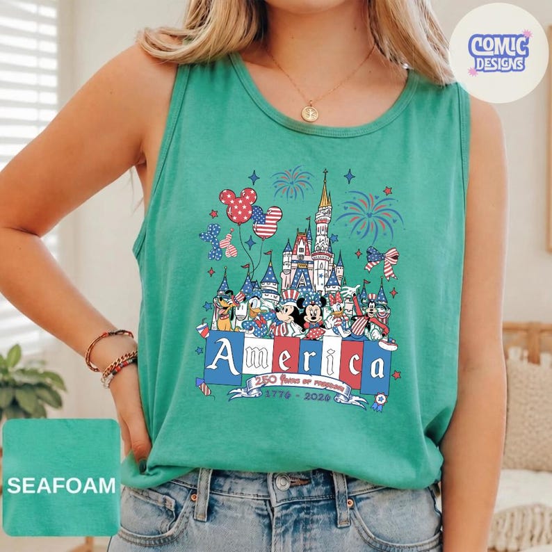 May include: A seafoam green sleeveless tank top featuring a graphic print of a castle, fireworks, and cartoon characters wearing patriotic red, white, and blue accessories. The text reads America, 250 Years of Freedom, 1776-2026 in a banner.