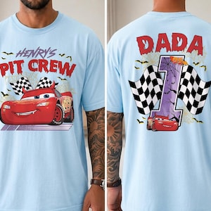 Puede incluir: Una camiseta azul claro con un gr&aacute;fico de coche de carreras rojo. El frente muestra el texto "HENRY'S PIT CREW" con banderas a cuadros y murci&eacute;lagos. La parte posterior muestra el texto "DADA" sobre un n&uacute;mero "1" grande con telara&ntilde;as y un coche.