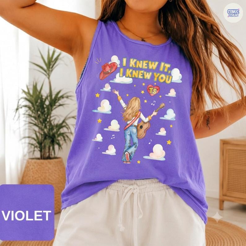 May include: A violet sleeveless tank top featuring a graphic print of a person with long blonde hair playing an acoustic guitar. The design includes the text "I KNEW IT, I KNEW YOU" in yellow, a red cowboy hat, white clouds, yellow stars, and a red heart.