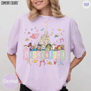 Pu&ograve; includere: T-shirt color orchidea con grafica Disneyland. Il design presenta un castello, personaggi dei cartoni animati e la scritta "Disneyland" in un font pastello. La maglietta ha maniche corte e una vestibilit&agrave; rilassata. Il marchio "COMFORT COLORS" &egrave; stampato in alto a sinistra.