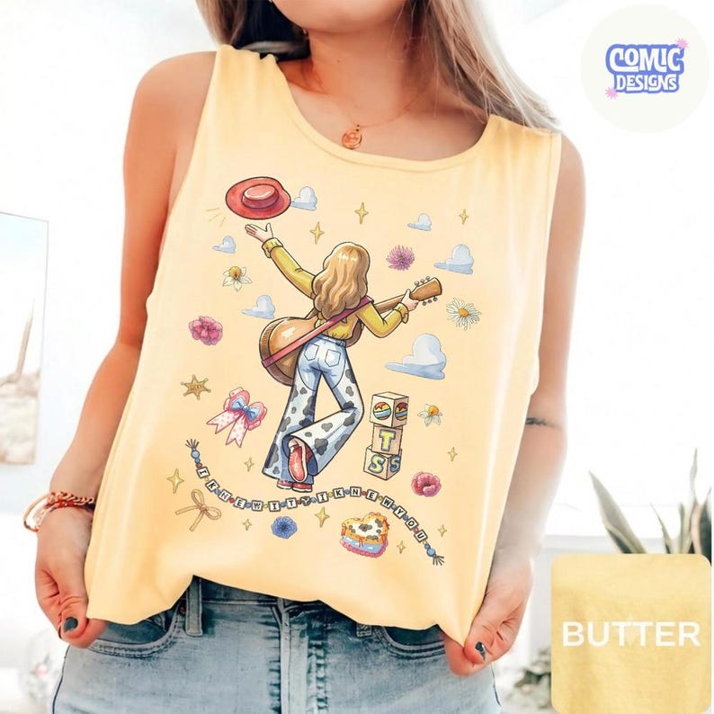 May include: A pale yellow sleeveless tank top featuring a graphic illustration of a person with long hair holding a guitar and a red hat. The design includes cow-print pants, stacked blocks with the letters T, S, and a heart, and text elements.