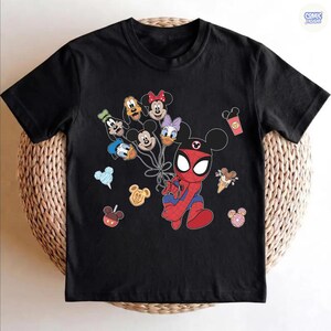 Peut inclure: T-shirt noir avec un personnage de Spider-Man de dessin anim&eacute; portant des oreilles de Mickey Mouse, tenant des ballons en forme de personnages Disney. D'autres graphismes sur le th&egrave;me de Disney incluent des cornets de glace, des beignets et une tasse de caf&eacute;. Le t-shirt a un col rond et des manches courtes.