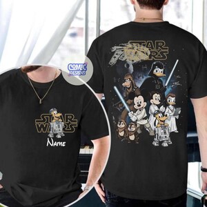 May include: Black t-shirt featuring a Star Wars-themed design with Disney characters. The front displays the Star Wars logo and a character with the name "Name" below. The back showcases various characters with lightsabers and the Star Wars logo.