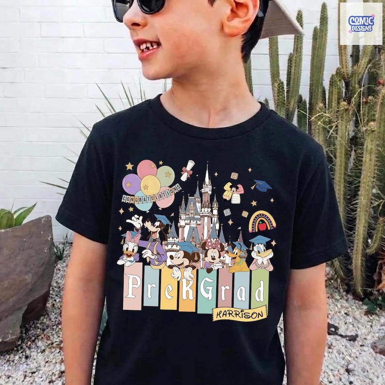 May include: Black t-shirt featuring a colorful graphic of Disney characters, a castle, balloons, and graduation elements. The shirt says "Prek Grad" and "Karrison". The design includes Mickey and Minnie Mouse, Donald and Daisy Duck, and other characters.