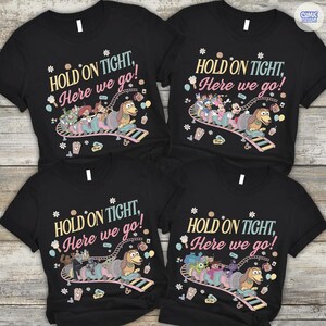 May include: Four black t-shirts with the phrase "HOLD ON TIGHT, Here we go!" in pastel colors. Each shirt features a different cartoon character train scene with Slinky Dog. The shirts are short-sleeved.