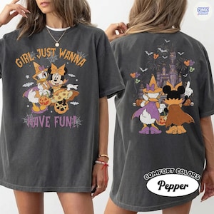 May include: A charcoal gray t-shirt featuring a Halloween-themed graphic of Daisy Duck and Minnie Mouse in costumes. The front displays the text "GIRL JUST WANNA HAVE FUN" with spiderwebs. The back shows the characters facing a castle with fireworks.