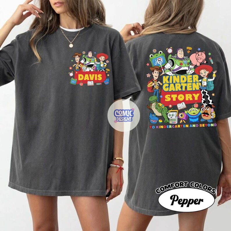 May include: A charcoal gray t-shirt featuring Toy Story characters on the front pocket area with the name DAVIS and a large back graphic with the text KINDERGARTEN STORY TO KINDERGARTEN AND BEYOND, showcasing Woody, Buzz Lightyear, and friends.