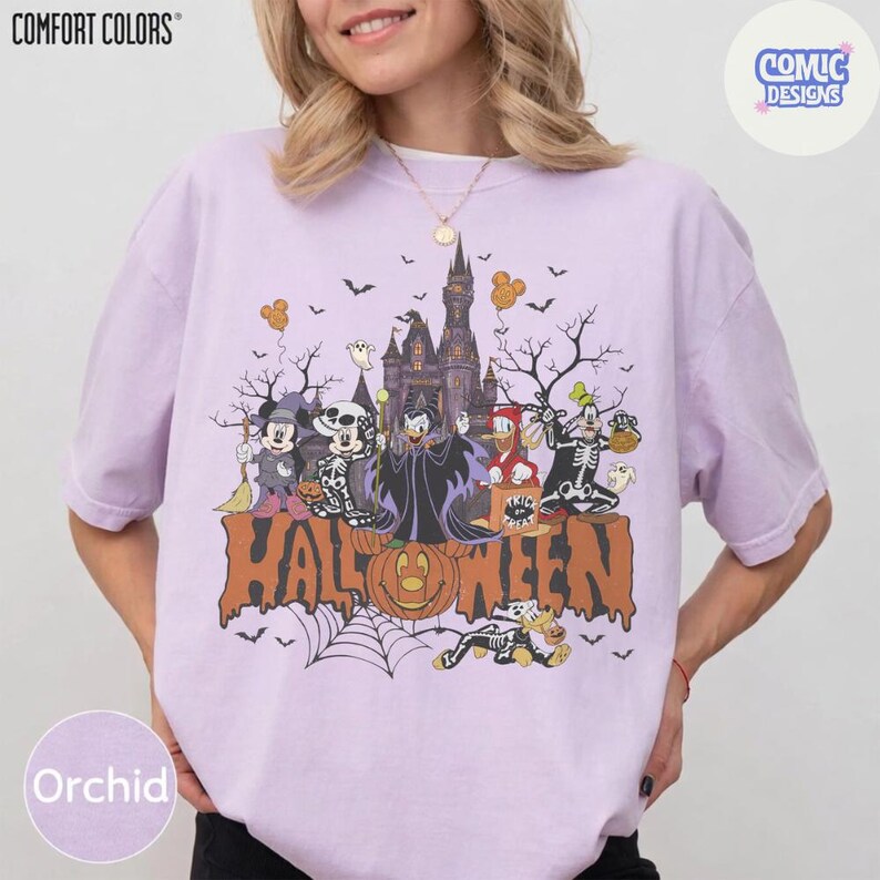 Puede incluir: Una camiseta de color morado claro con un gr&aacute;fico de personajes de Disney disfrazados de Halloween frente a un castillo. El texto HALLOWEEN est&aacute; impreso en letras grandes de color naranja en la parte inferior. Incluye a Mickey, Minnie y Goofy.