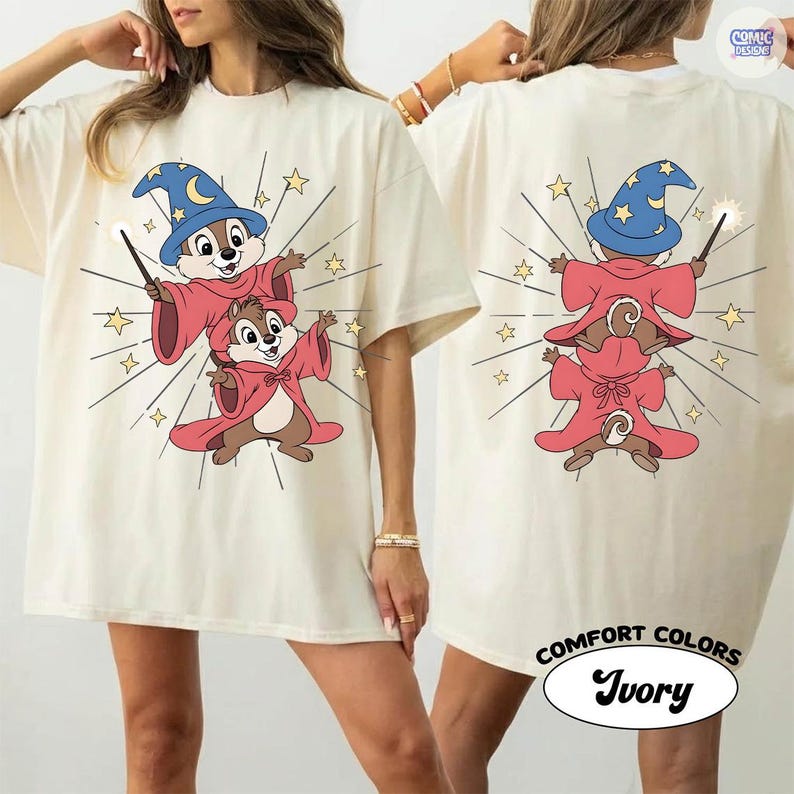 Puede incluir: Camiseta de color marfil con un dise&ntilde;o de mago de dibujos animados en la parte delantera y trasera. El dise&ntilde;o incluye dos ardillas listadas con t&uacute;nicas rojas y sombreros de mago azules, sosteniendo varitas. La camiseta tiene las palabras "COMFORT COLORS" e "Ivory".