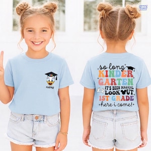 May include: Light blue t-shirt with a Donald Duck graphic wearing a graduation cap and the text "NAME". The back of the shirt says "so long KINDERGARTEN, IT'S BEEN MAGICAL, LOOK OUT, 1ST GRADE +here i come!+"