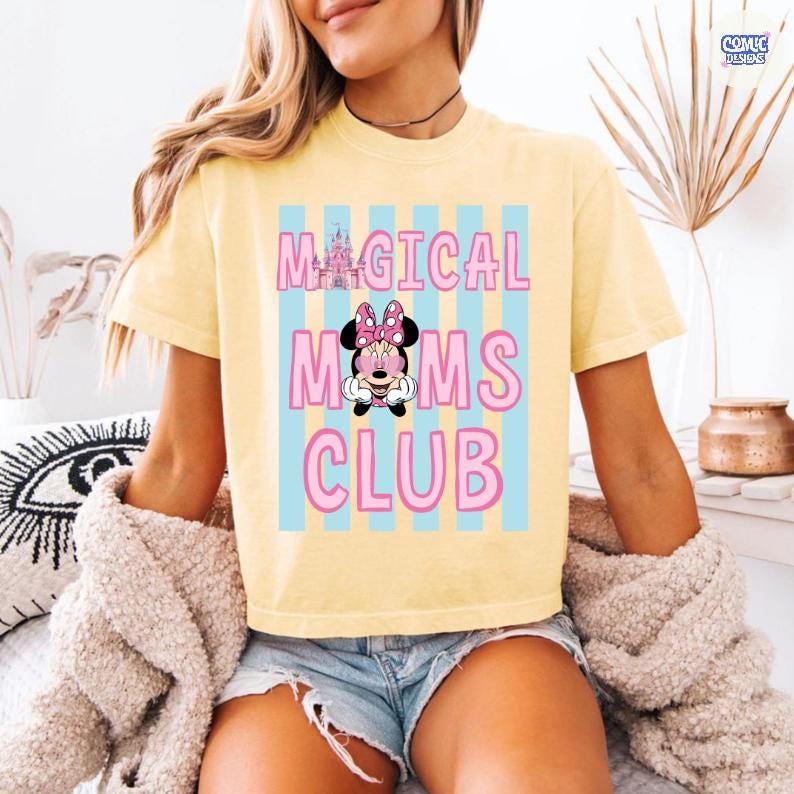 K&ouml;nnte beinhalten: Gelbes T-Shirt mit dem Text "MAGICAL MOMS CLUB" in Pink, mit einer Minnie Mouse Grafik. Das Shirt hat blaue vertikale Streifen hinter dem Text. Das Shirt ist kurz&auml;rmlig.