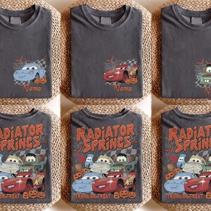 May include: A collection of dark grey t-shirts featuring Disney Pixar Cars characters in Halloween costumes. Some shirts show individual cars with the text Name, while others display the full group with the text Radiator Springs Trunk or Treat.