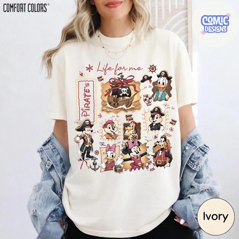 May include: Ivory-colored t-shirt featuring a pirate-themed design with cartoon characters. The design includes a pirate ship, skull, and various characters in pirate attire. The text "Life for me" and "Pirate's" are also visible.