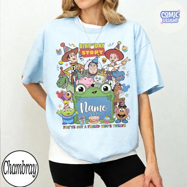May include: A light blue t-shirt featuring a colorful graphic of various animated toy characters wearing party hats. The text reads Birthday Story, Name, and You've Got A Friend Who's Twelve. A small logo in the top right corner says Comic Designs.