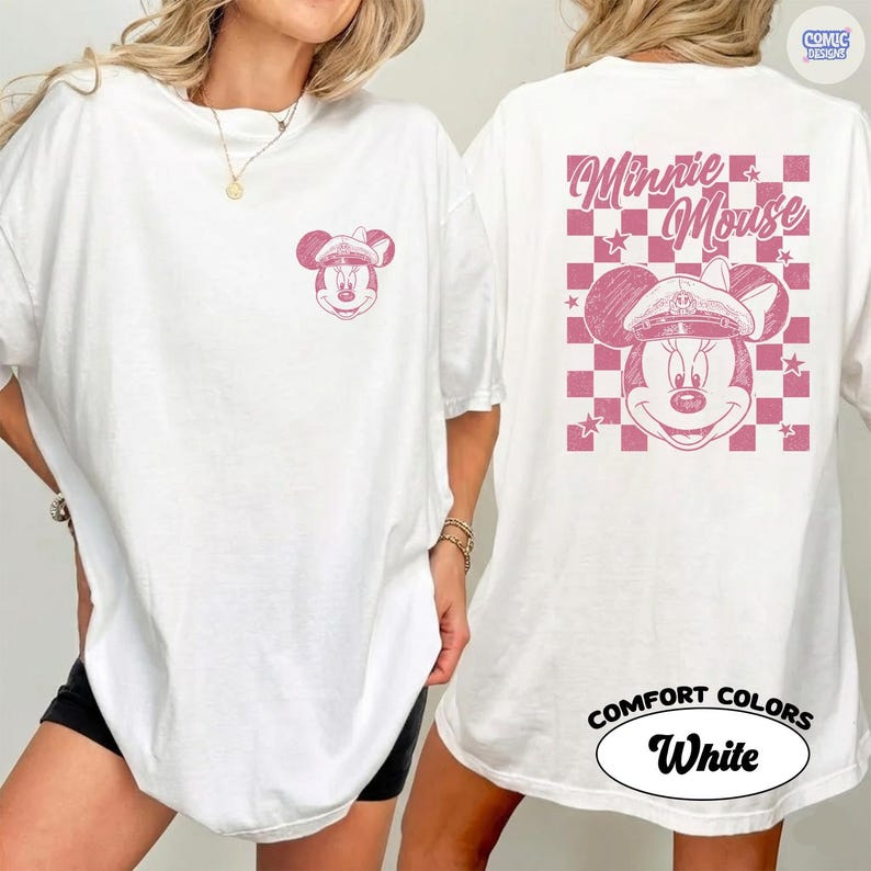 May include: White t-shirt with a pink Minnie Mouse graphic. The front has a small Minnie Mouse design, and the back features a larger design with the words "Minnie Mouse" and a pink and white checkered pattern. The shirt is labelled "Comfort Colors White."