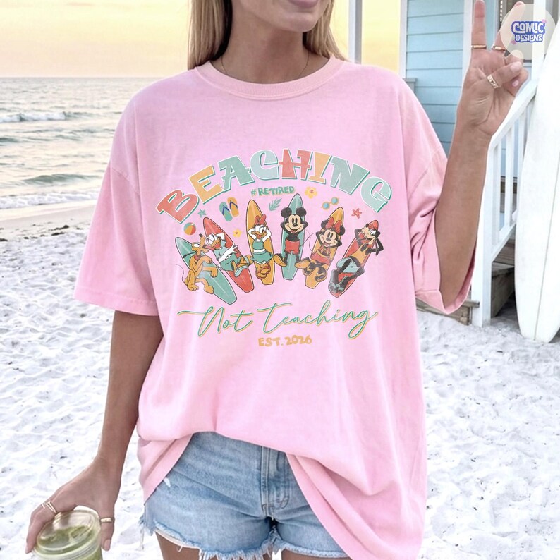 May include: A pink t-shirt with the words "BEACHING Not Teaching" in colorful letters and a graphic of cartoon characters on surfboards. The shirt also has the text "#Retired EST. 2026".