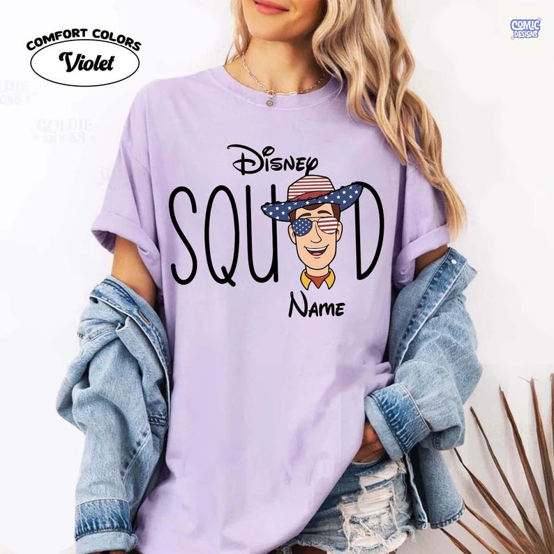 May include: A violet Comfort Colors t-shirt with a Disney Squad design. The graphic features Woody from Toy Story wearing a patriotic hat and sunglasses. The word "Name" is below the character.