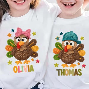 Könnte beinhalten: Weiße T-Shirts mit Cartoon-Truthahn-Designs. Ein Truthahn trägt eine rosa Schleife, der andere eine blaue Kappe. Beide haben bunte Federn und Sterne. Die Namen "Olivia" und "Thomas" sind darunter aufgedruckt.