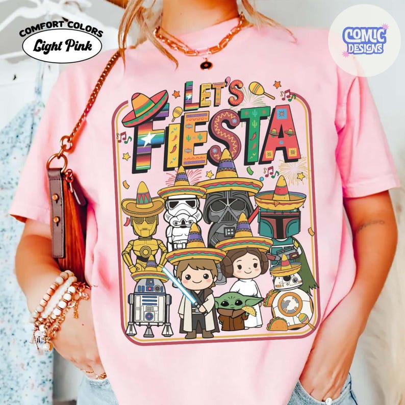 May include: Light pink Comfort Colors t-shirt with a graphic that says "Let's Fiesta". The graphic features cartoon characters wearing sombreros. The characters include C-3PO, R2-D2, Darth Vader, and Baby Yoda.