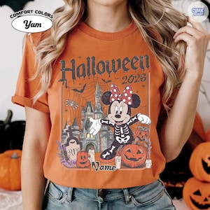 May include: Orange t-shirt with a Halloween graphic. The design includes Minnie Mouse in a skeleton costume, a haunted castle, pumpkins, and the text "Halloween 2026". The shirt has the Comfort Colors and Comic Designs logos.