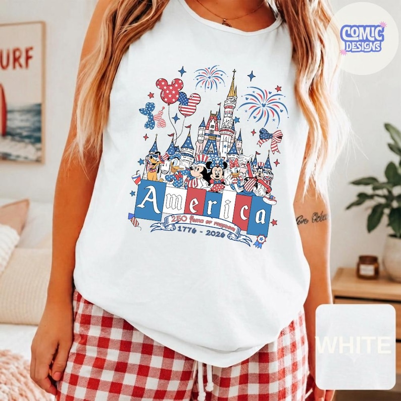 May include: A white sleeveless tank top featuring a graphic print of a castle, fireworks, and cartoon characters wearing patriotic red, white, and blue outfits. The text reads America, 250 years of freedom, and 1776-2026 in a stylised font.