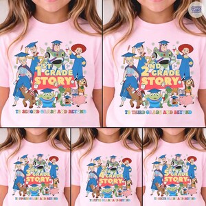 May include: Pink t-shirts with a colorful graphic featuring characters from the movie Toy Story. Each shirt displays a grade level from 1st to 5th grade, with the text "STORY" and "TO SECOND GRADE AND BEYOND" or similar phrases.