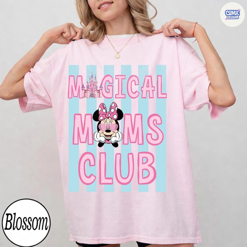 K&ouml;nnte beinhalten: Hellrosa T-Shirt mit dem Schriftzug "MAGICAL MOMS CLUB" in Pink, mit einer Minnie Mouse Grafik. Der Text ist vor einem Hintergrund aus hellblauen vertikalen Streifen platziert. Eine Burg-Grafik befindet sich &uuml;ber dem Wort "MOMS".
